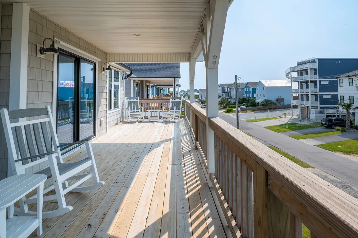 This image captures a welcoming exterior porch with classic rocking chairs and a wooden railing, offering an open view of the surrounding seaside houses. The atmosphere is tranquil and inviting, ideal for sipping morning coffee or enjoying the ocean breeze.