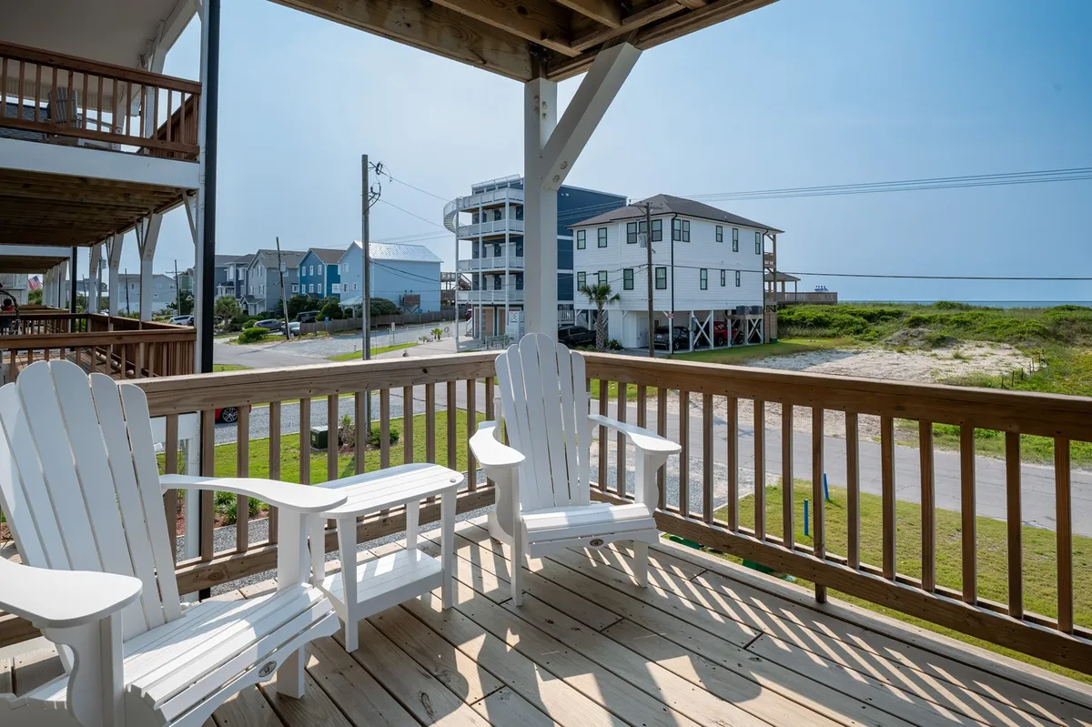 A serene snapshot of a green lawn with white Adirondack chairs, blue sky, and views of surrounding houses. The space feels open and inviting, ideal for relaxing while keeping an eye on kids or pets at play.