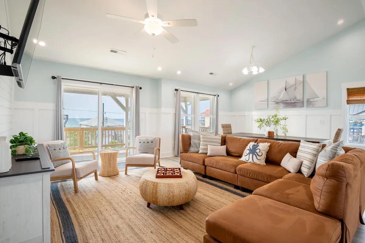 A large and inviting Great Room features a spacious sectional sofa, a woven coffee table, a ceiling fan overhead, and expansive windows that frame views of the outdoors. The layout encourages gatherings and relaxation, while the abundant natural light highlights the room's open, airy atmosphere.