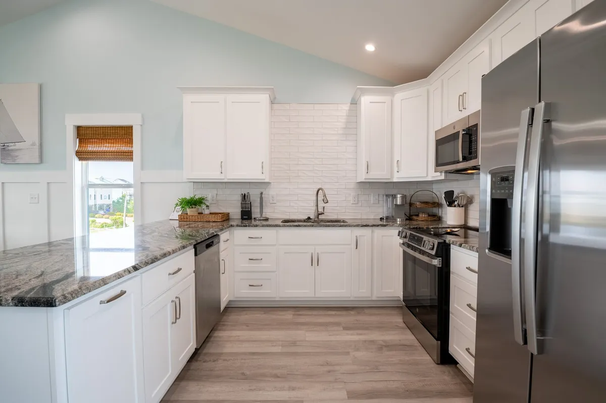 The kitchen is outfitted with granite countertops, stainless steel appliances, white cabinetry, and a textured backsplash. The scene feels both modern and welcoming, perfect for cooking and entertaining with family or friends.