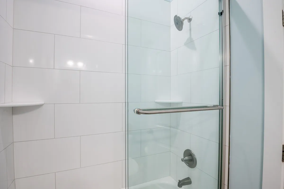 A modern bathroom shower with a glass enclosure, white tile, and updated shower fixtures. The scene feels fresh, bright, and clean, capturing the custom tile shower amenity.