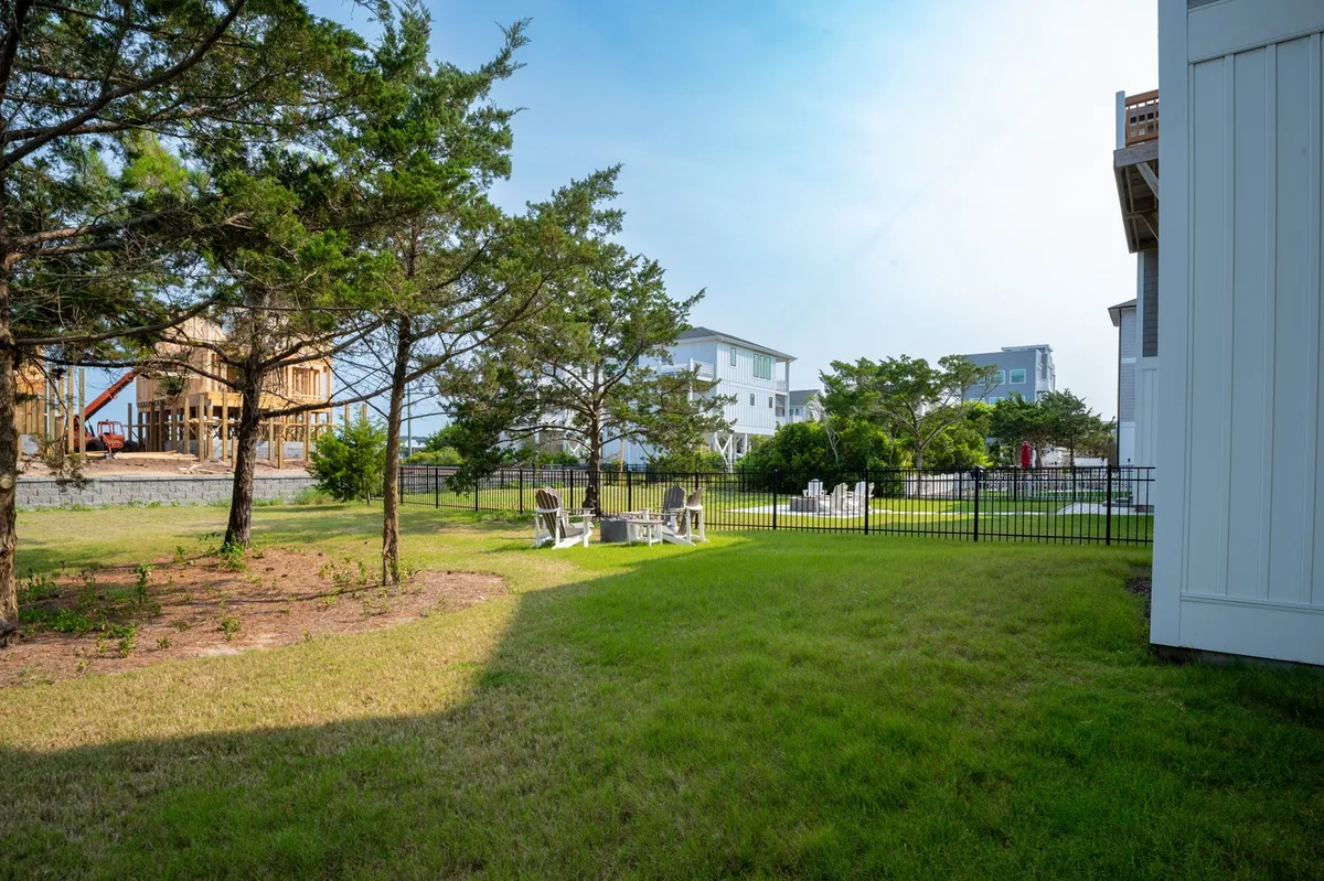 A wide lawn area with comfortable seating arrangements is surrounded by leafy trees and a fenced perimeter, offering ample space for kids and pets to play safely or for family gatherings and outdoor games.