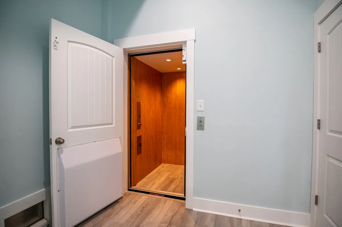 This interior image features an open elevator (cargo lift) with wood paneling inside and light-colored walls surrounding it. The view clearly emphasizes the elevator's modern convenience and clean design. The elevator is empty, reinforcing its practical purpose for moving items between floors.