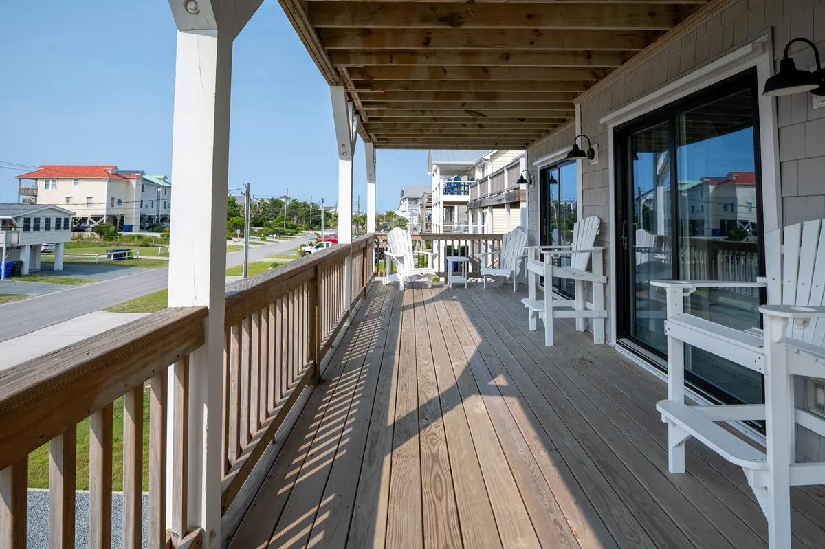 An inviting wooden deck with white Adirondack chairs overlooks the street, creating a social space perfect for relaxing, enjoying a coffee, or chatting with family while enjoying fresh air and scenic views.