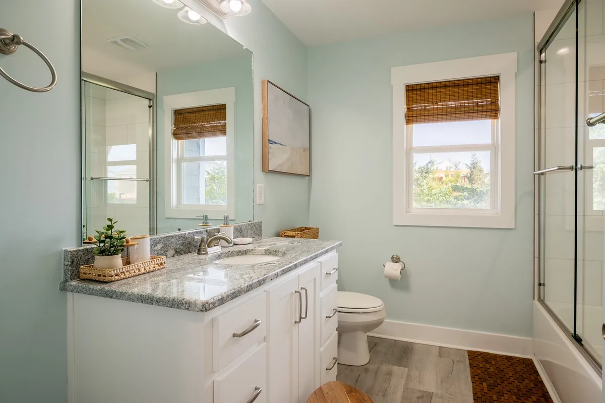 This bathroom scene displays a vanity with a granite countertop, a large mirror, and a window allowing in soft natural light. The space feels calm and inviting, with upgraded finishes that provide a sense of luxury for daily routines.