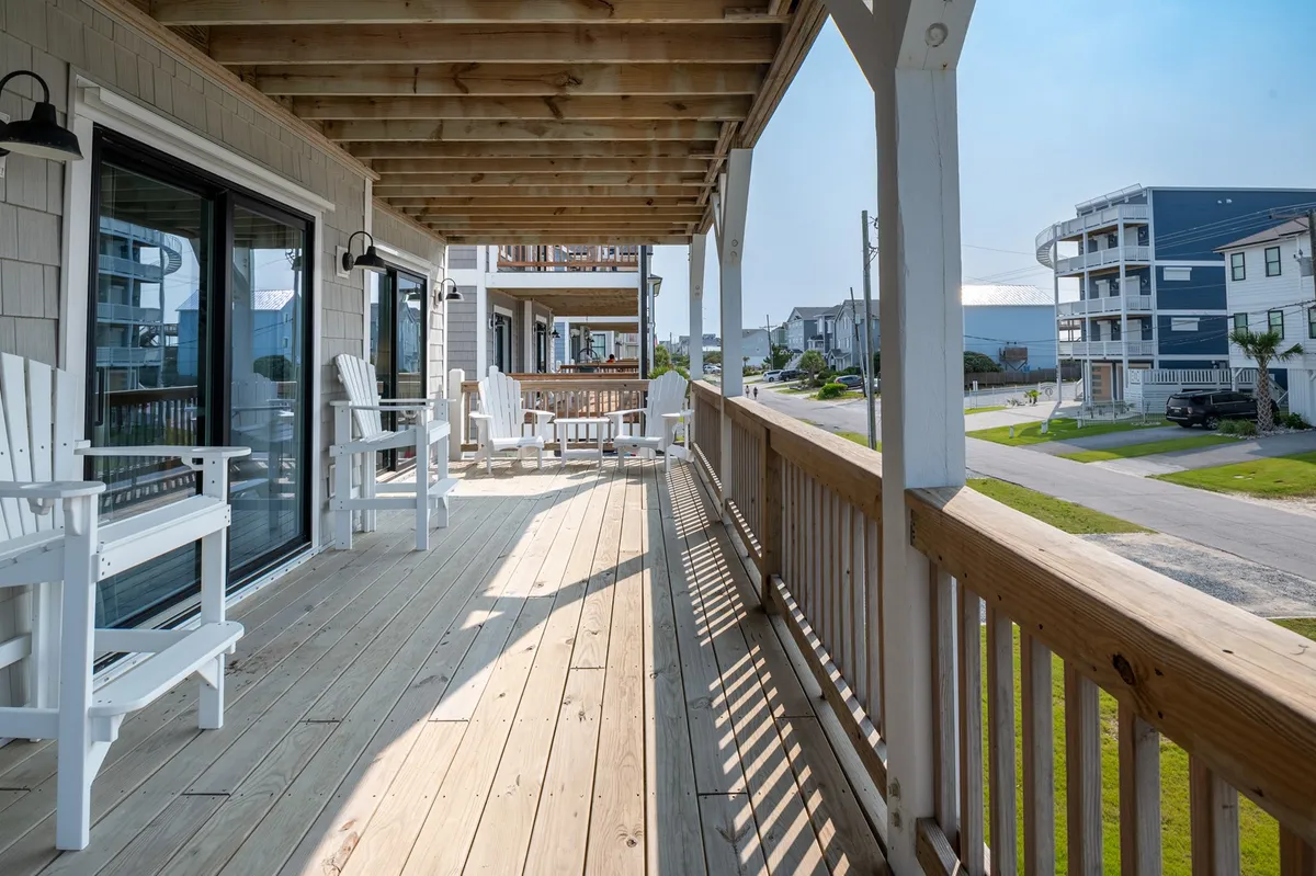 Featuring white Adirondack chairs set on a wooden deck, this exterior image overlooks nearby houses, immersing guests in the tranquil outdoor setting. The space is perfect for unwinding, reading, or enjoying sunset cocktails while listening to the waves.