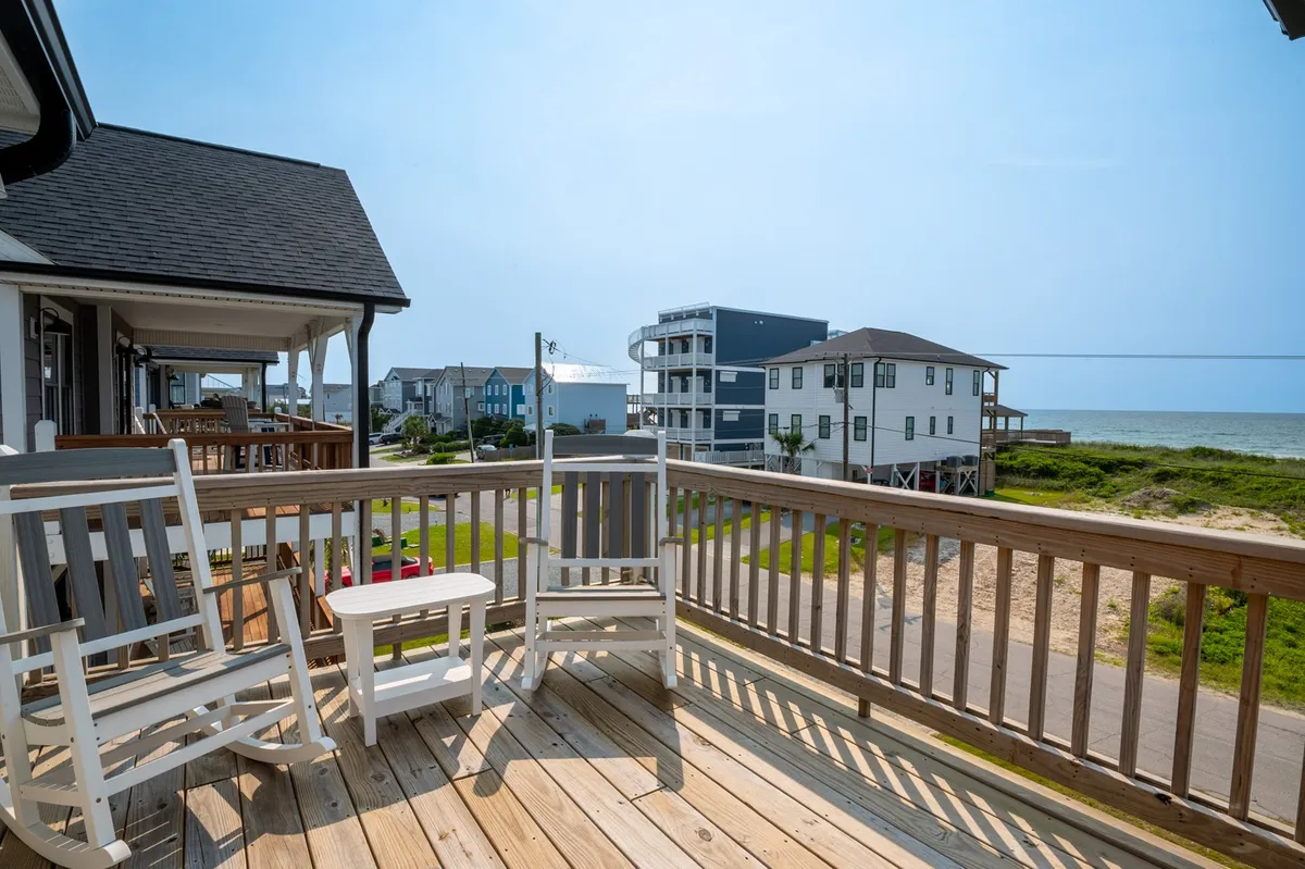 A tranquil porch scene presents rocking chairs arranged on a deck facing a stunning ocean view. The space is ideal for unwinding, enjoying ocean breezes, and soaking in sunrise or sunset vistas.